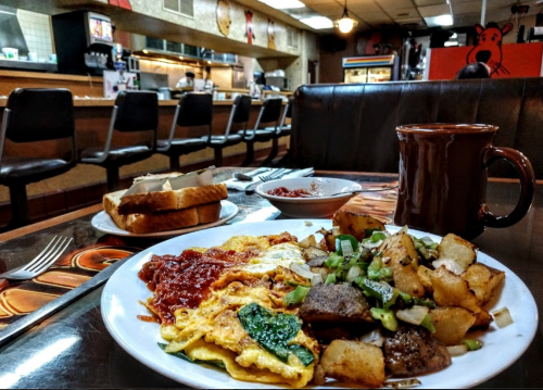 A plate of omelette with salsa, potatoes, and toast, with a coffee cup in a cozy diner setting.
