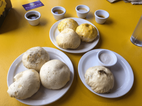 Two plates of steamed buns with dipping sauces on a bright yellow table.