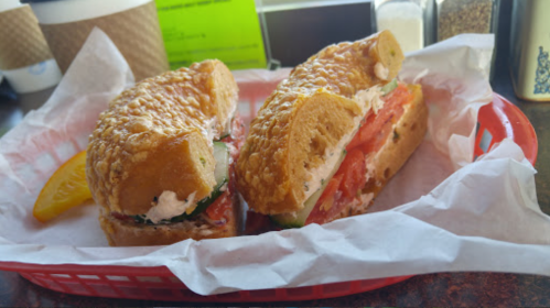 A sandwich on a red tray, featuring layers of tomato, lettuce, and a creamy spread, with a lemon wedge on the side.