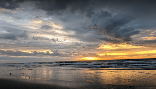 A serene beach at sunset, with waves gently lapping the shore and dramatic clouds in the sky.
