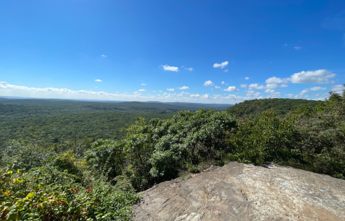 A panoramic view of lush green hills under a clear blue sky with scattered clouds.