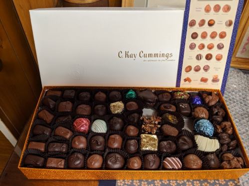A beautifully arranged box of assorted chocolates with various shapes and colors, featuring a decorative lid.