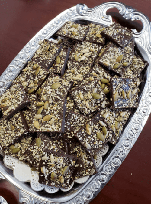 A silver platter filled with chocolate bark topped with seeds and nuts, arranged in neat squares.
