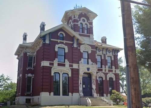 A large, ornate Victorian-style house with red and white exterior, featuring intricate architectural details and a tower.