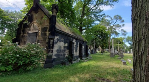 A historic stone mausoleum surrounded by trees and gravestones in a serene cemetery setting.