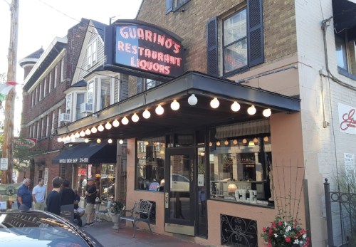 A charming restaurant and liquor store with a neon sign, outdoor seating, and people gathered outside.
