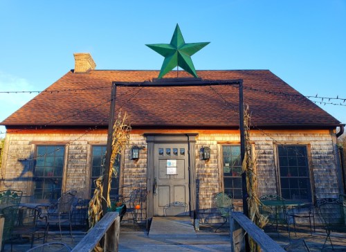 A rustic wooden building with a green star on the roof, surrounded by outdoor seating and a clear blue sky.