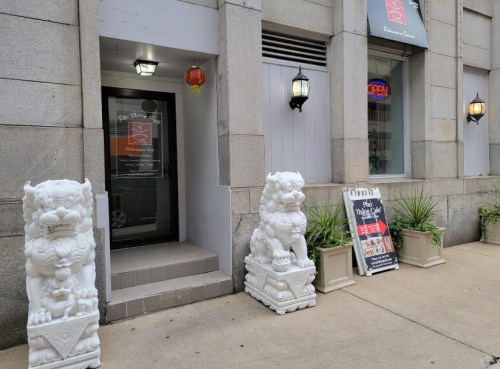 Entrance of a building featuring two white lion statues, lanterns, and a signboard displaying various promotions.