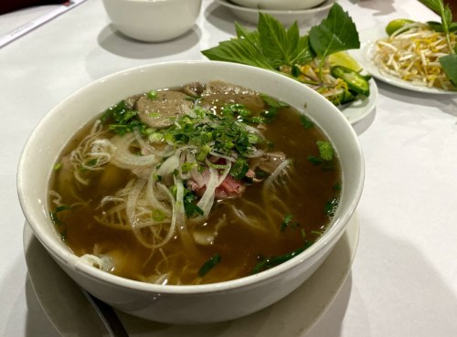 A bowl of pho with noodles, herbs, and meat, served with fresh lime and bean sprouts on the side.