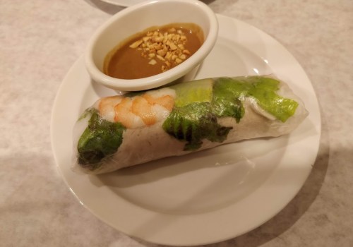 A fresh spring roll with shrimp and lettuce, served on a plate with a side of peanut dipping sauce.