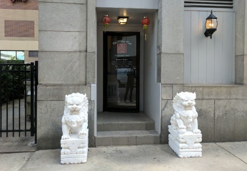 Entrance with two white lion statues flanking a door, lanterns hanging above, and a stone facade.