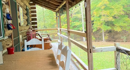 A cozy porch with a wooden table and chairs, surrounded by trees with autumn foliage.