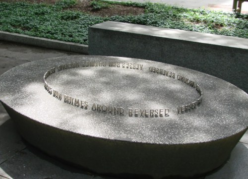 A curved stone bench with engraved text that reads "Reversed rhymes around reversed." Surrounded by greenery.