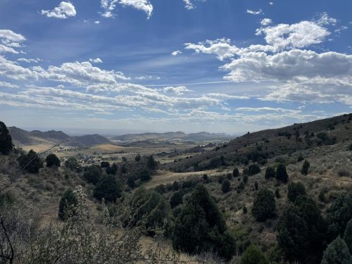A scenic view of rolling hills and valleys under a partly cloudy sky, with greenery in the foreground.