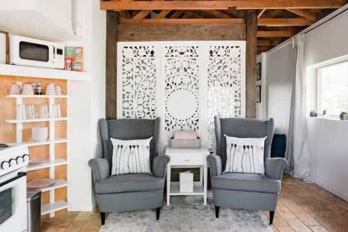 Cozy living space featuring two gray armchairs, a small table, and a decorative screen against a rustic backdrop.