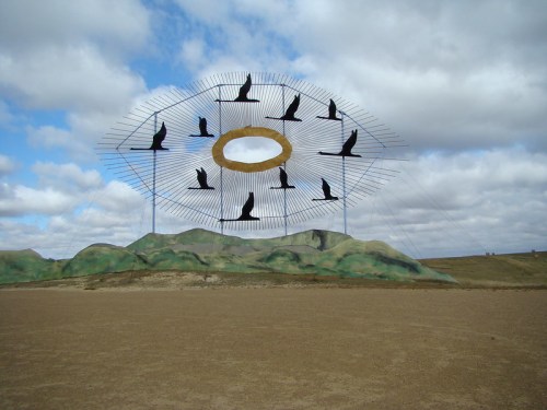 A large sculpture featuring birds in flight, set against a cloudy sky and grassy landscape.