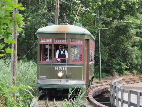 A vintage green streetcar labeled "Desire" travels along a curved track surrounded by lush greenery.