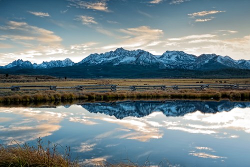 A serene landscape featuring snow-capped mountains reflected in a calm pond under a colorful sky.