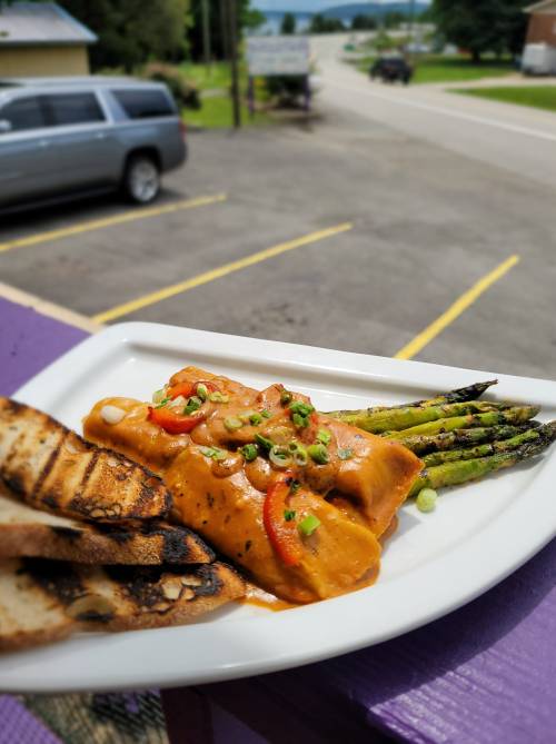 A plate of grilled chicken enchiladas topped with sauce, served with grilled asparagus and toasted bread, outdoors.