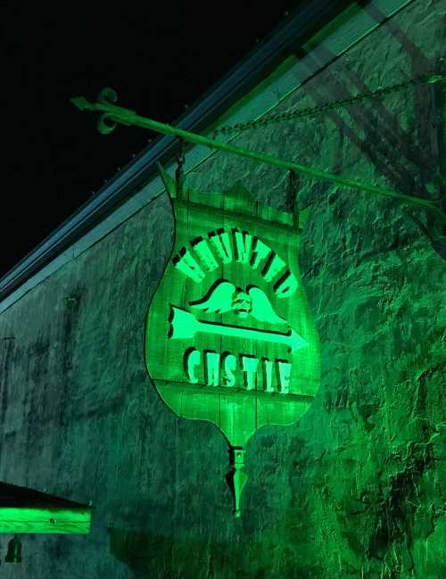 A green-lit sign reading "Haunted Castle" hangs from a building at night.