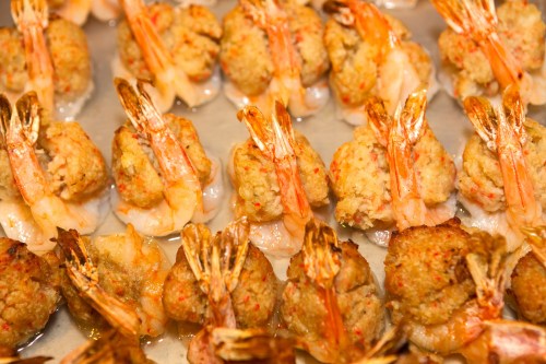 A close-up of baked stuffed shrimp arranged neatly on a tray, showcasing their golden-brown topping and pink shrimp.