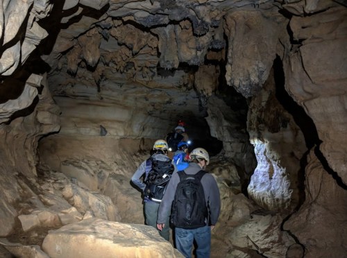 A group of people with helmets exploring a dark cave, illuminated by headlamps and natural rock formations.