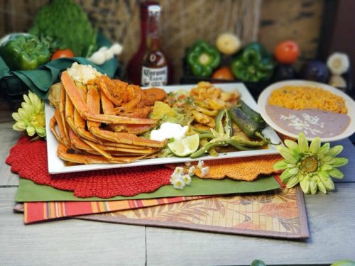 A vibrant platter of seafood, including crab legs and shrimp, served with sides of rice and vegetables, garnished with lime.