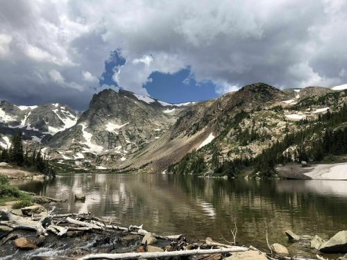 A serene mountain lake surrounded by rugged peaks and lush greenery under a partly cloudy sky.