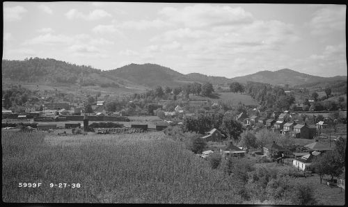 A scenic view of a rural landscape with hills, houses, and fields under a partly cloudy sky.