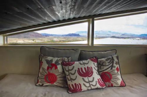 Cozy interior with decorative pillows and a scenic view of mountains and water through a triangular window.