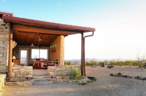 A rustic desert home with a stone exterior, open porch, and scenic mountain views in the background.