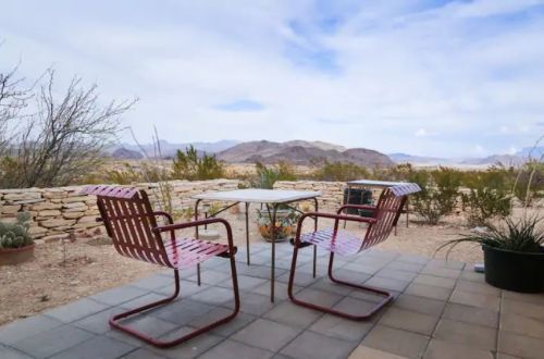 Two red chairs and a small table on a patio, overlooking a desert landscape with mountains in the distance.