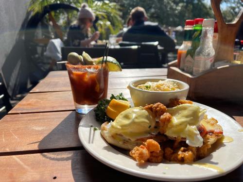 A plate of eggs Benedict with a side of mashed potatoes and a cocktail on a wooden table, with diners in the background.