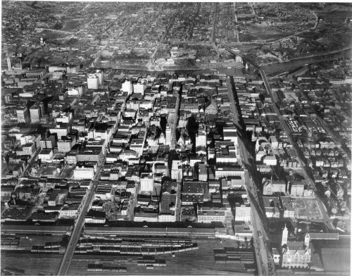 Aerial view of a city with buildings, streets, and train tracks, captured in black and white.