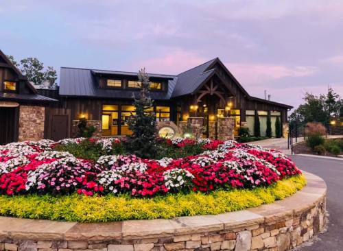 A charming lodge surrounded by vibrant flower beds at sunset, featuring a stone facade and a welcoming entrance.