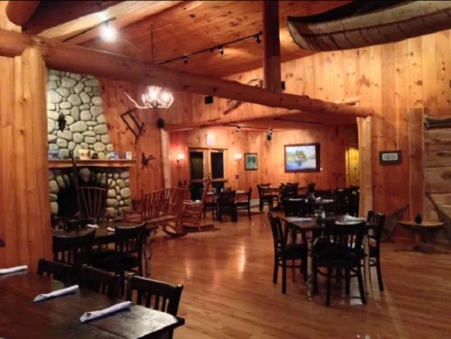 Cozy wooden restaurant interior with stone fireplace, wooden tables, and rustic decor. Warm, inviting atmosphere.