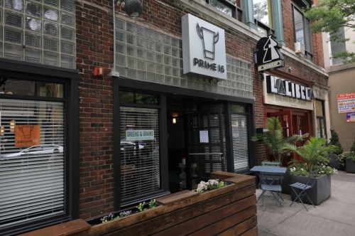 Exterior view of a restaurant named "Prime 16," featuring large windows and a brick facade, with outdoor seating.