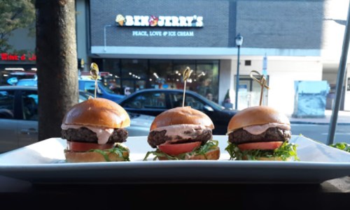 Three mini burgers on a white plate, with lettuce and tomato, in front of a Ben & Jerry's store.