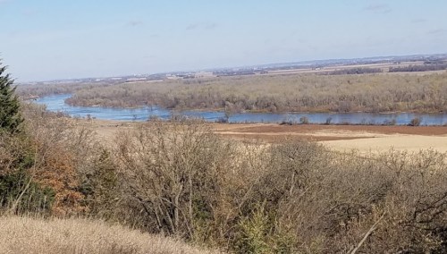 A scenic view of a winding river surrounded by trees and fields under a clear blue sky.