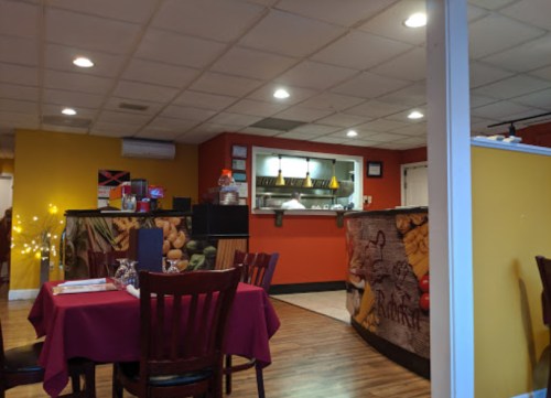 Cozy restaurant interior with red and yellow walls, wooden tables, and a visible kitchen area in the background.