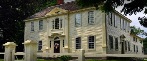 A large, historic yellow house with white trim, featuring multiple windows and a decorative entrance.