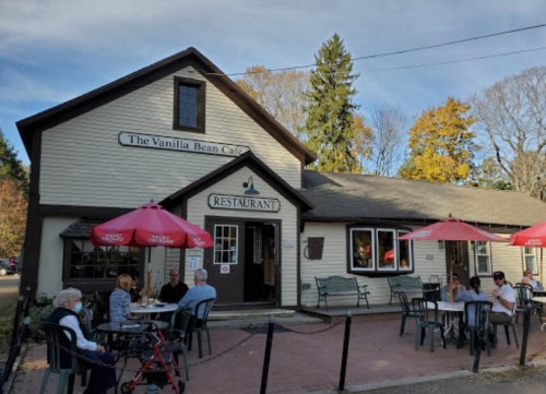 A cozy restaurant with outdoor seating, red umbrellas, and autumn trees in the background.