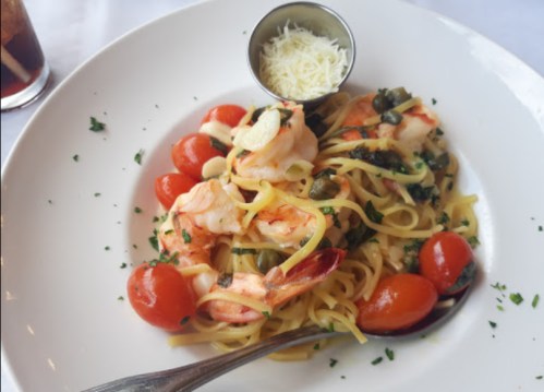 A plate of shrimp pasta with cherry tomatoes, capers, and a side of grated cheese.