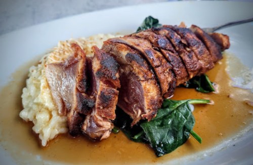 Sliced roasted duck on a bed of creamy risotto and spinach, drizzled with a savory sauce.