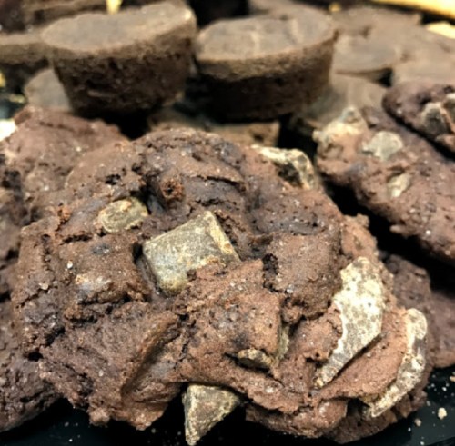 A close-up of chocolate cookies with chunks of chocolate, stacked on a dark plate.