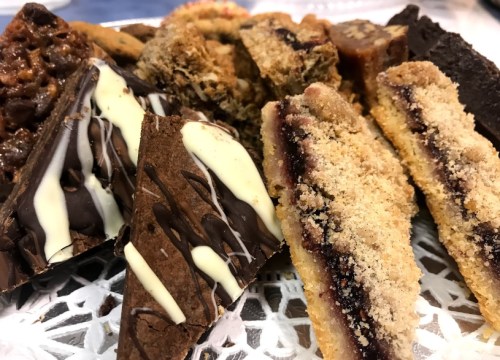 A variety of delicious desserts, including chocolate bars and layered treats, arranged on a lace doily.