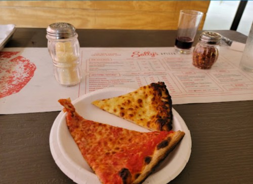Two slices of pizza on a paper plate, one with cheese and the other with sauce, on a table with condiments.