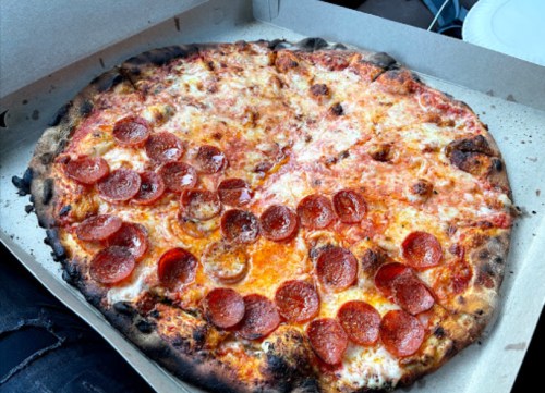 A pepperoni pizza with melted cheese and a charred crust, placed in a pizza box.