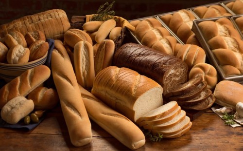 A variety of freshly baked breads, including loaves, rolls, and baguettes, arranged on a wooden table.