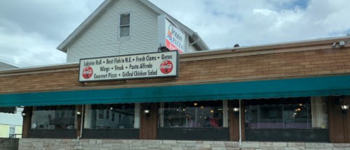 A restaurant exterior featuring a sign with menu items like lobster roll, wings, and grilled chicken salad.